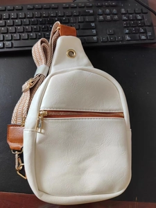 Detail shot of white pebbled leather chest bag showing brown zipper and jacquard strap