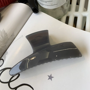 Detail view of a translucent dark grey hair claw clip with a glossy finish on white paper