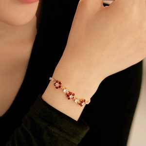 Detail of a gold flower bracelet with red gems on a woman's wrist in a luxury setting