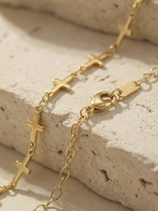 Detailed close-up of golden cross chain bracelet with lobster clasp on natural stone background
