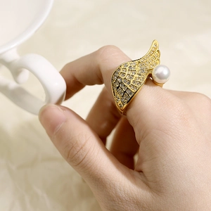 Detailed close-up of a golden angel wing ring with pavé crystals and a white pearl on finger