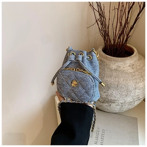 Detailed close-up of blue denim mini bucket bag with gold camellia charm and chain strap