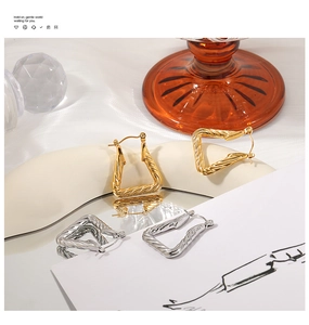 Detail shot of gold and silver twisted rope triangle hoop earrings on silk display