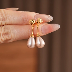 Detail showing teardrop pink pearl earrings with hammered gold spheres held by hand