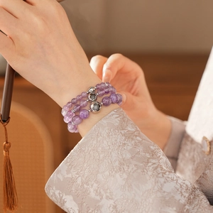 Detail of layered purple amethyst bracelet with silver flower charm on a model's wrist