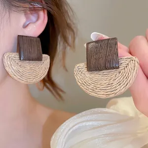 Detail of bohemian rattan earrings featuring wooden square studs and woven semi-circles