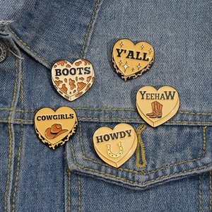Set of five heart-shaped cowboy enamel pins with western motifs on denim jacket
