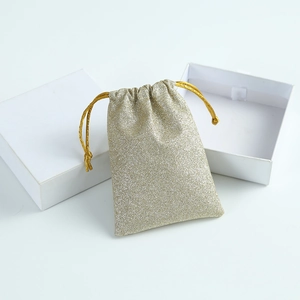 Close-up of glitter gold drawstring jewelry pouch and premium white gift box on clean background
