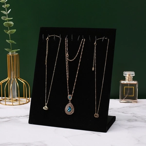 Vertical black velvet necklace display stand with metal hooks on marble surface