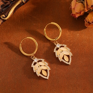 Detailed view of gold leaf earrings with beige cat eye stone and diamonds on brown suede