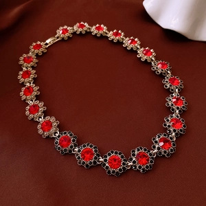 Close-up of red and black floral gemstone necklace links on a silk fabric background