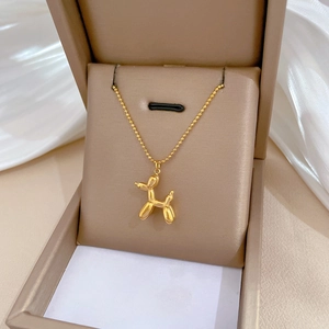 Golden 3D balloon dog pendant necklace in a beige gift box on white fabric background