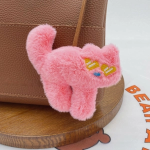 Detailed close-up of a pink plush cat charm with heart eyes on a leather bag