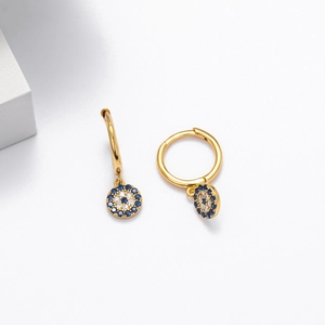 Macro shot of gold huggie hoop earrings featuring evil eye charms with blue zircon stones