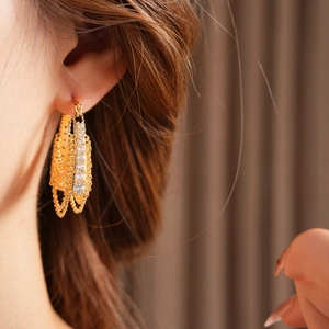 Close-up of gold plated chain earrings with zircons worn by model on a brown backdrop