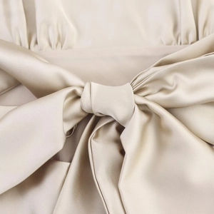 Détail macro de robe en satin champagne montrant l'éclat du tissu et le nœud élégant