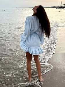 Detail of light blue V-neck dress featuring ruffled hem and soft chiffon fabric on a beach