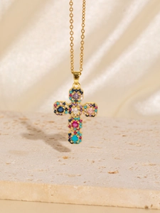 Macro shot of gold cross pendant necklace with colorful zircon stones on textured base