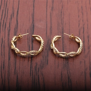 Gros plan de boucles d'oreilles C torsadées dorées avec zircons sur fond de bois