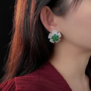 Elegant emerald flower stud earrings with sparkling diamonds on a model's ear