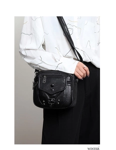 Détail du sac bandoulière noir avec texture litchi, fermetures éclair et rivets décoratifs