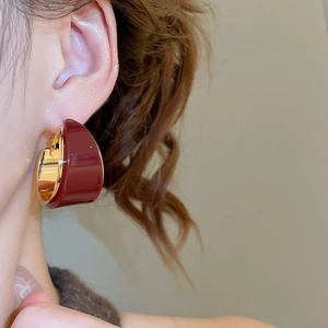 Gros plan de boucles d'oreilles en C dorées 18K avec résine bordeaux sur modèle