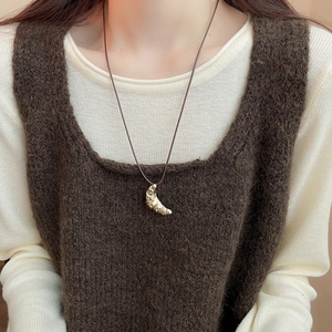 Close-up of golden croissant pendant necklace on brown leather cord over knit vest