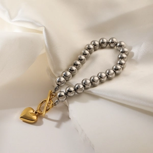 Silbernes Perlenarmband mit goldenem Herzanhänger und Knebelverschluss auf Seidenstoff