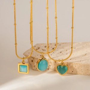 Three gold necklaces with square, round, and heart blue cat-eye pendants on stone