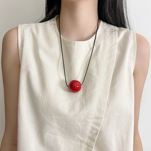 Detail of a round red sphere pendant on a thin black cord worn with a beige top