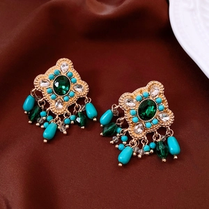 Macro detail of vintage bohemian earrings with green crystals and blue beaded tassels