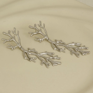 Macro shot of silver coral branch earrings on a beige ceramic plate with soft lighting