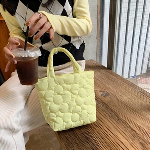 Detail of yellow quilted tote bag with floral stitching held by a model on a wooden bench