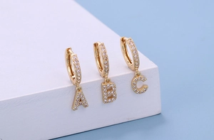 Detailed close-up of golden hoop earrings featuring white zircon letters A B and C