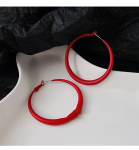 Close-up of red matte hoop earrings on a minimalist white tray and black background