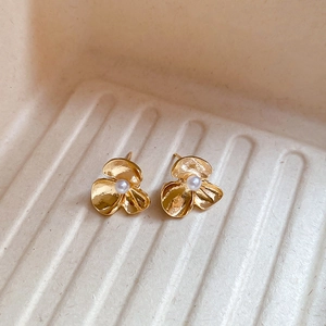 Detail of flower stud earrings with gold finish and central pearl on a white tray