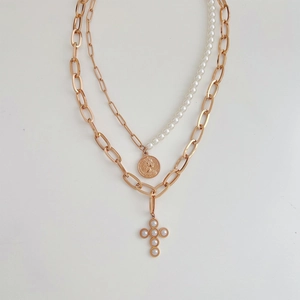 Double-layered gold portrait coin and pearl cross necklace on a white background