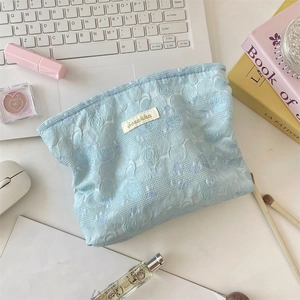 Detail of light blue lace toiletry bag with 3D flower texture on a desk setup