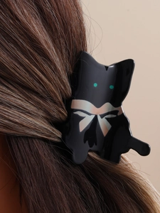 Detail showing an abstract black cat hair claw clip with bow pattern on brown hair