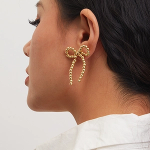 Detail of golden beaded bow earring with imitation pearls on a model ear