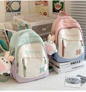 Detail of color-block student backpacks with cute plush rabbit charms on a desk