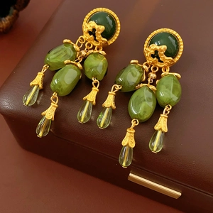 Close-up of vintage gold earrings with intricate hollow carvings and green teardrop pendants