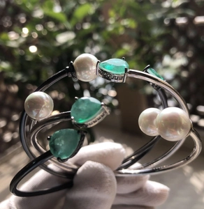 Detail of silver bangles featuring white pearls and green pear-cut gemstones