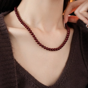 Close-up of a vintage dark red beaded titanium steel necklace worn on a brown knit sweater
