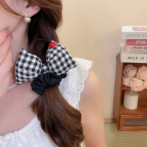 Detail of checkered bow hair tie with red heart accent worn in a low ponytail style