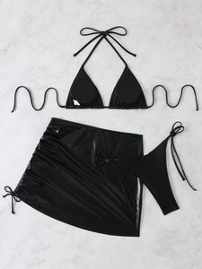 Detailed flat lay of a black shiny three-piece bikini set with mini skirt on marble
