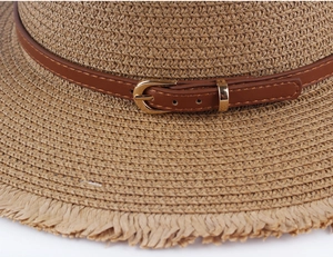 Close-up of woven straw hat featuring a brown leather band and golden buckle detail