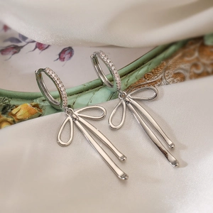 Detailed view of silver bow earrings with crystals resting on elegant white silk fabric