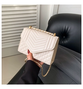 Detail of cream quilted chain bag with V-pattern stitching and gold metal strap
