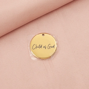 Close-up of golden stainless steel Child of God engraved round pendant on pink fabric